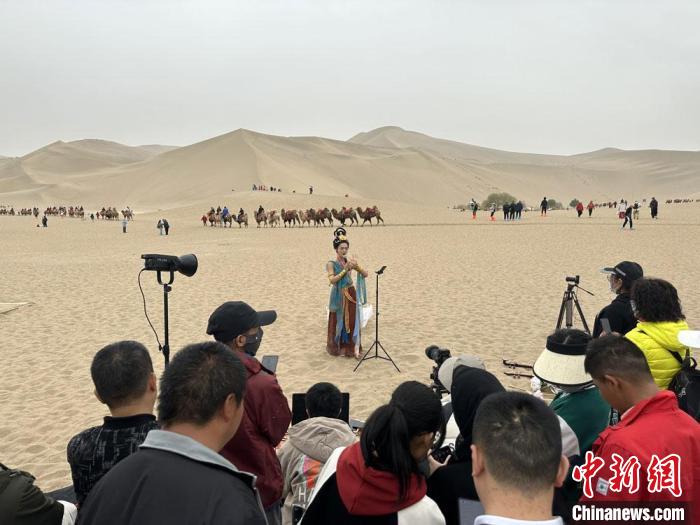 圖為2023年4月底，敦煌大漠“逐舞者”奧楠在鳴沙山月牙泉景區(qū)視頻直播，吸引游人圍觀。　馮志軍 攝